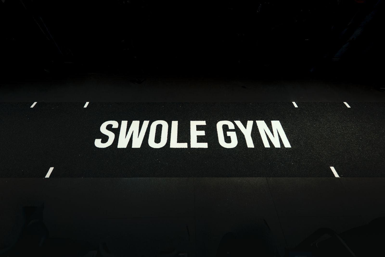 The SWOLE GYM branded training floor under low light